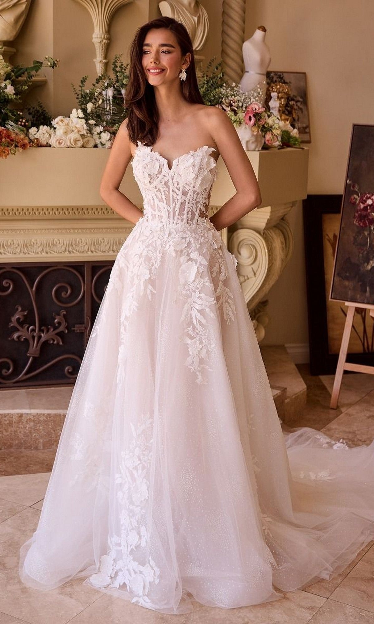 A woman stands indoors smiling with her hands on her waist, wearing the Long Wedding Dress: Andrea and Leo WL018—a strapless lace gown with a sweetheart neckline and long tulle skirt.